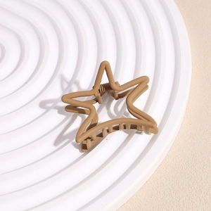 Close-up of matte khaki star-shaped hair claw clip with a strong metal spring on a tray