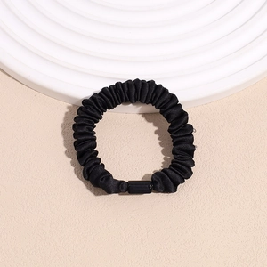 Close-up of black pleated satin scrunchie on elegant white minimal presentation display