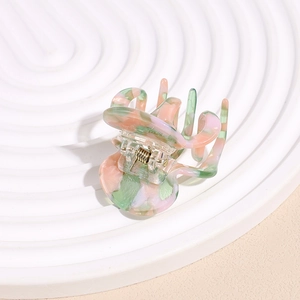 Pince à cheveux en acétate marbré rose et vert sur un support de présentation ondulé