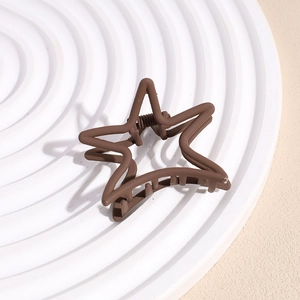 Close-up of matte brown star-shaped hair claw clip on white textured display board
