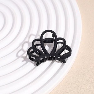 Close-up of small matte black claw clip with crown shape design on textured background