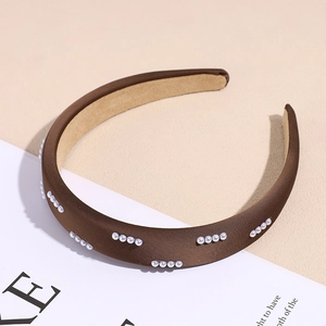 Dettaglio di un elegante cerchietto in raso marrone con piccole perle bianche