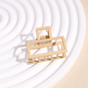 Detail of a matte beige rectangular hair claw clip with a strong metal spring on a white tray