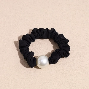 Close-up of black pleated hair tie with a large white pearl detail on a beige surface