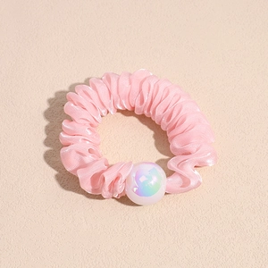 Detail of pink ruffled organza scrunchie with iridescent pearl bead on beige texture