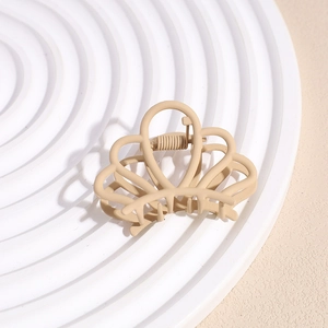 Matte beige crown-shaped hair claw clip with hollow design on a round display tray