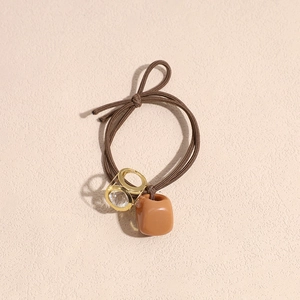 Close-up of brown elastic hair tie with faceted crystal pendant and resin cube charm