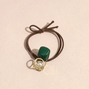 Macro detail of brown elastic hair tie with green resin square and gold rhinestone charm