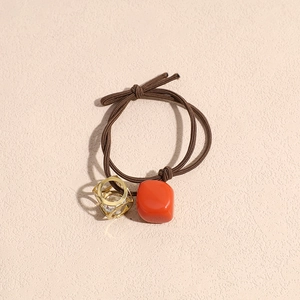 Detailed macro view of brown elastic hair tie with red square bead and gold hollow pendant