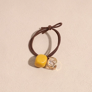 Detail of a brown woven hair tie featuring a yellow cube bead and a hollow gold pendant