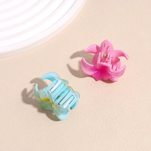 Floral frangipani hair claw clips in matte pink and teal blue on a textured sand background