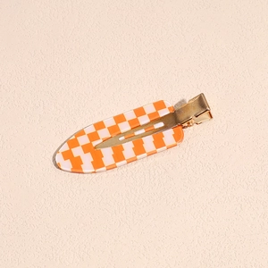 Dettaglio di un fermaglio per capelli a scacchi arancione e beige con retro in metallo