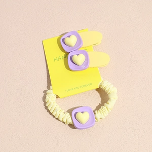 Détail de pinces à cheveux carrées violettes et chouchou jaune avec motifs de cœur en résine