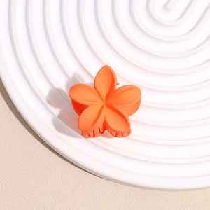 Détail macro d'une petite pince à cheveux fleur orange sur un plateau blanc texturé