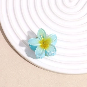 Macro detail of blue plumeria hair claw clip with yellow gradient on a beach textured tray