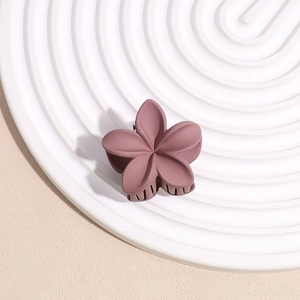 Détail d'une pince à cheveux fleur mate violette sur un plateau ondulé blanc élégant
