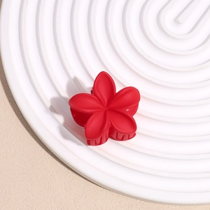 Vue détaillée d'une petite pince à cheveux fleur rouge mat sur un plateau blanc