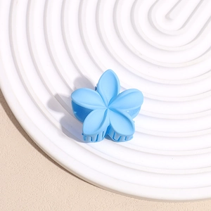 Gros plan d'une pince à cheveux fleur bleue mate sur un plateau de présentation blanc