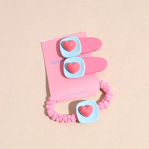 Détail de l'ensemble de barrettes à cœur rose et bleu et chouchou sur carton rose