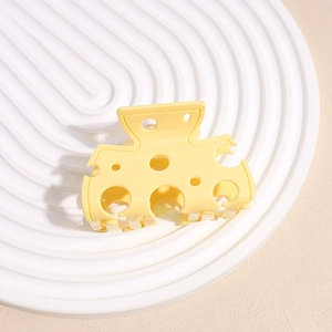 Detailansicht einer gelben Käse-Haarklammer aus Acryl auf einem weißen runden Keramikteller