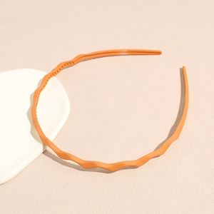 Close-up of orange wavy headband with inner teeth design on minimalist background