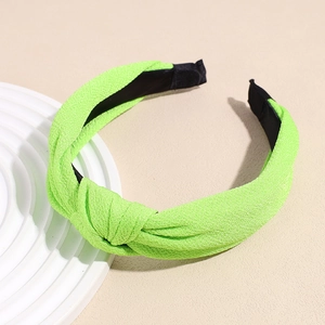 Detail of neon green knotted headband with rich textured fabric on a white display board