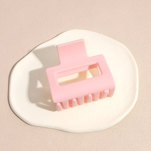 Close-up of matte pink square hair claw clip on a minimalist white display board