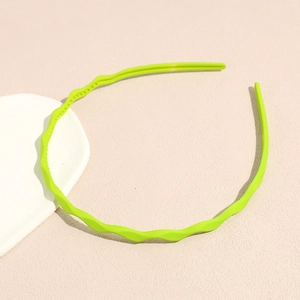 Close-up of bright neon green wavy headband with anti-slip teeth on a soft pink background