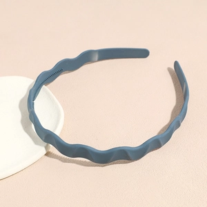 Detail of matte blue wavy headband showing non-slip inner teeth on soft beige surface