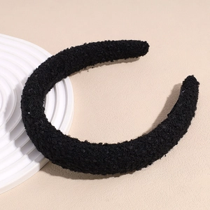 Détail d'un bandeau épais en peluche noire texture laine d'agneau sur un socle blanc