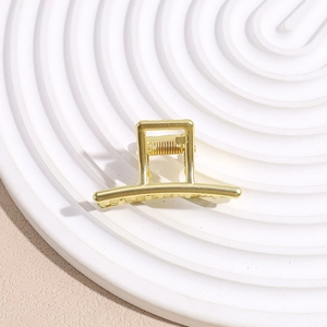 Macro shot of a minimalist gold metal shark hair claw clip on a white spiral plate