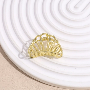Macro detail of a shell-shaped matte gold metal hair claw clip with cutout design