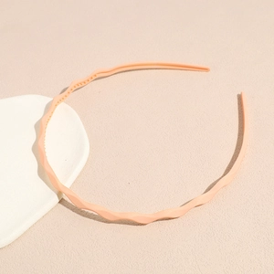 Detailed macro view of a slim wavy candy-colored hairband in matte peach pink plastic finish