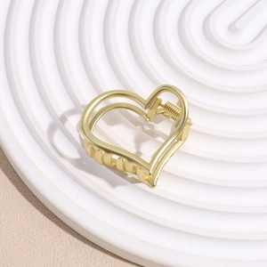 Detail of matte gold heart-shaped claw clip showing the spring mechanism and hollow design