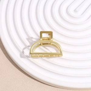 Close-up of a matte gold minimalist metal hair claw clip on a white ceramic display tray