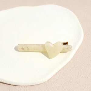 Détail de la pince à cheveux beige marbré avec cœur sur une assiette en céramique blanche