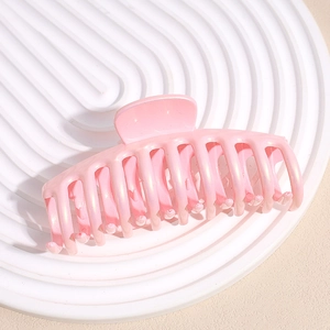 Close-up of a large pearlescent pink shark hair claw clip on a white textured tray