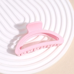 Detail view of large matte pink hair claw clip on a white decorative tray with elegant shadows