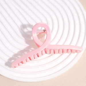 Top macro view of large pink matte shark hair claw clip on white ripple pedestal