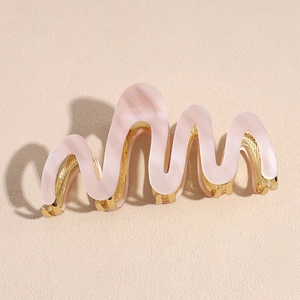 Detailed close-up of pink marble acetate hair claw clip with wave design and golden metal finish