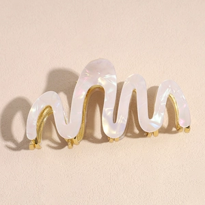 Detail of the elegant wavy hair claw clip with pearlescent finish and golden metal base