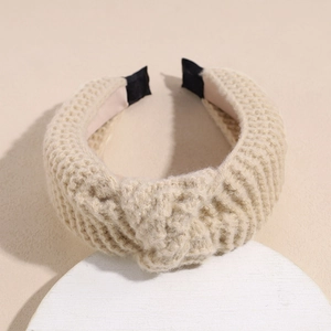 Detail of beige knitted headband featuring a top knot and thick woven fabric texture