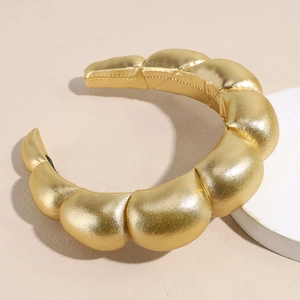 Dettaglio del cerchietto imbottito in oro metallizzato con design a segmenti e texture