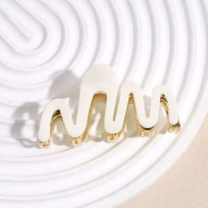Detailed view of cream acetate hair claw with golden metal wavy design and texture