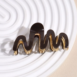 Close-up of wavy brown acetate hair claw clip with golden metal teeth and spring mechanism