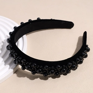 Detailed view of black velvet wide headband with assorted black beads on beige surface