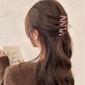 Brown acetate hair claw clip with wave design on model's dark curly hair in warm lighting