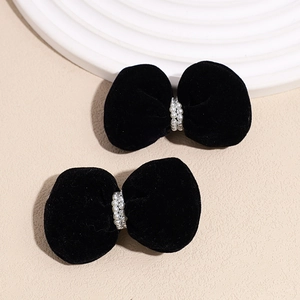 Close-up of black velvet bow hair clips with faux pearl center on textured surface