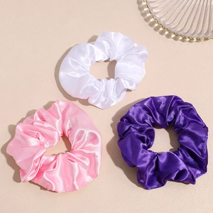 Tre elastici LED in raso nei colori bianco, rosa e viola su uno sfondo beige caldo