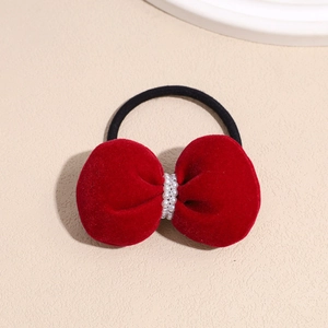 Close-up of red velvet bow hair tie with rows of white pearls on beige background